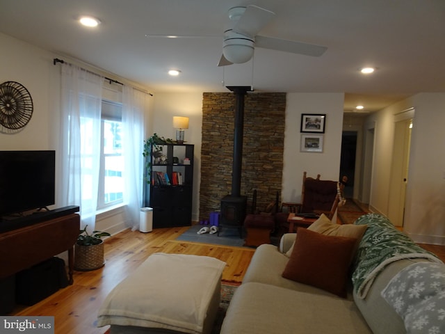 living room featuring a wood stove, ceiling fan, and light hardwood / wood-style flooring