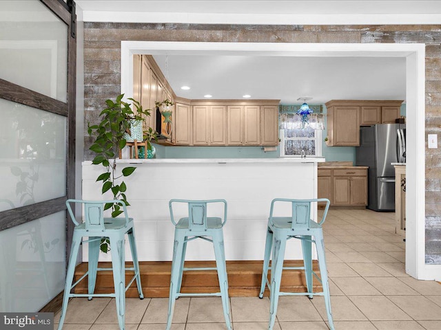 kitchen featuring a breakfast bar, light brown cabinetry, light tile patterned floors, stainless steel fridge, and a barn door