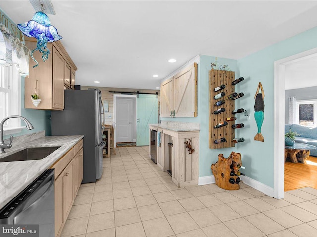 kitchen with light brown cabinetry, sink, stainless steel fridge, dishwashing machine, and a barn door