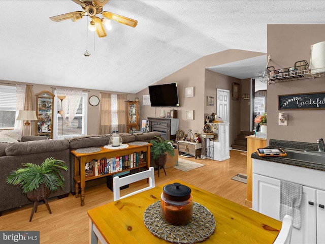 living room featuring ceiling fan, vaulted ceiling, light hardwood / wood-style flooring, and a textured ceiling