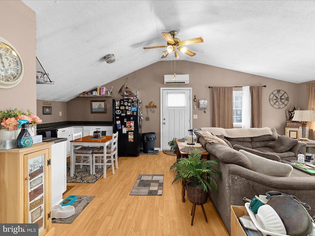 living room with lofted ceiling, ceiling fan, a wall unit AC, light hardwood / wood-style floors, and a textured ceiling