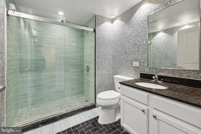 bathroom featuring toilet, tile walls, vanity, a shower with door, and backsplash