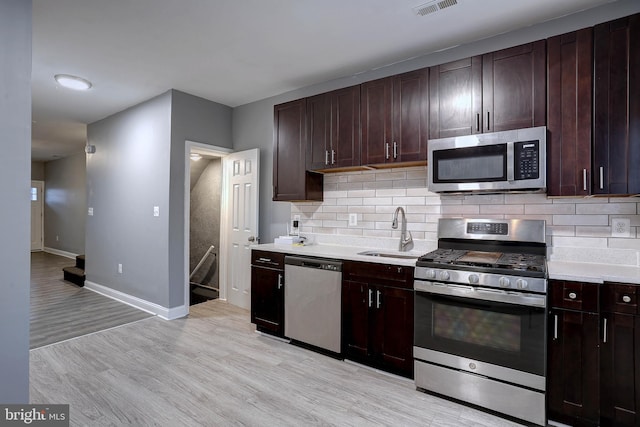 kitchen with appliances with stainless steel finishes, light hardwood / wood-style floors, sink, and backsplash