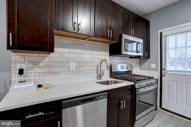 kitchen featuring appliances with stainless steel finishes, tasteful backsplash, sink, light stone counters, and light hardwood / wood-style floors