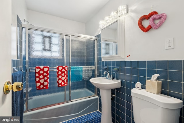 bathroom with tile walls, combined bath / shower with glass door, and toilet