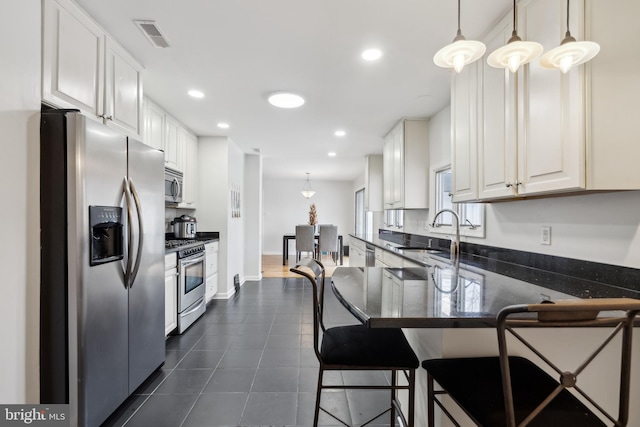 kitchen featuring appliances with stainless steel finishes, a breakfast bar, decorative light fixtures, sink, and white cabinets