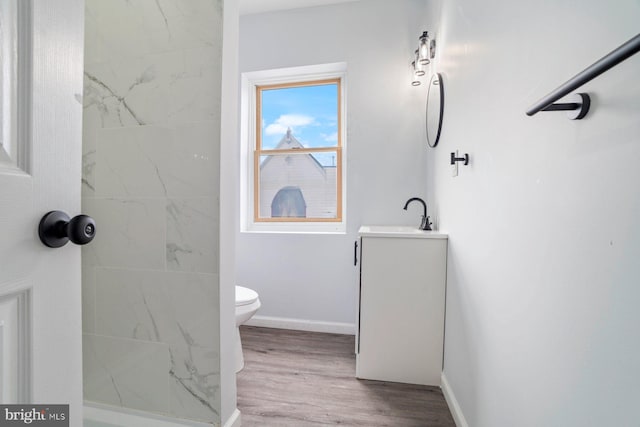 bathroom featuring vanity, wood-type flooring, a tile shower, and toilet