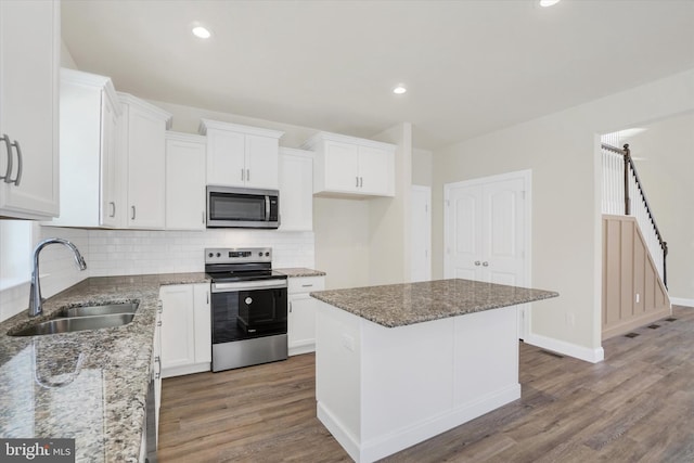 kitchen featuring sink, appliances with stainless steel finishes, white cabinetry, a center island, and stone countertops