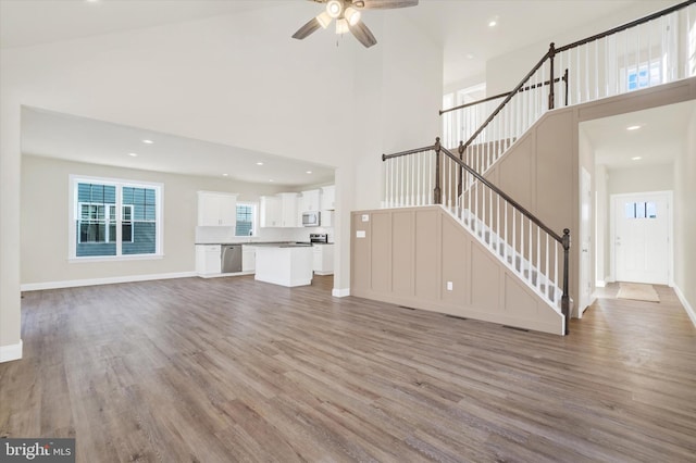 unfurnished living room featuring light hardwood / wood-style floors, ceiling fan, and a high ceiling