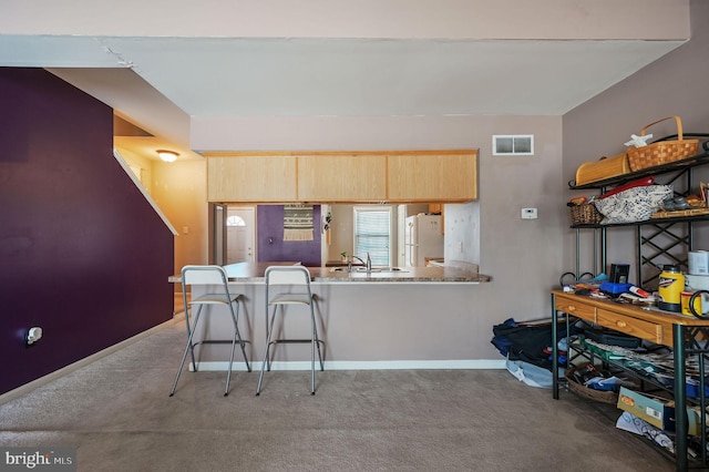 kitchen featuring light brown cabinetry, a breakfast bar area, white fridge, kitchen peninsula, and light carpet