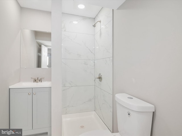 bathroom with a tile shower, vanity, and toilet