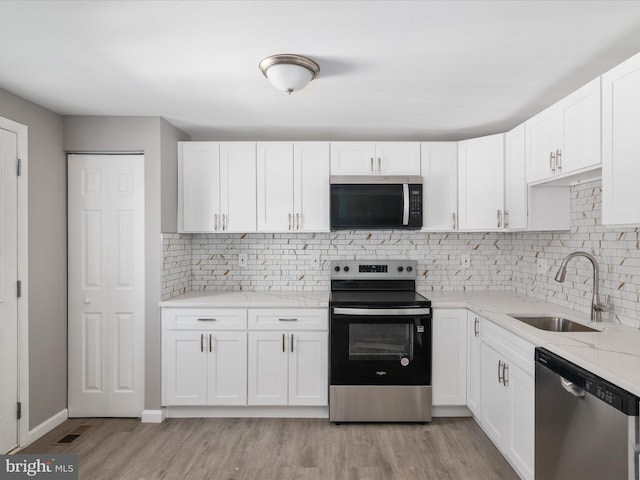 kitchen with stainless steel appliances, white cabinetry, sink, and light hardwood / wood-style flooring