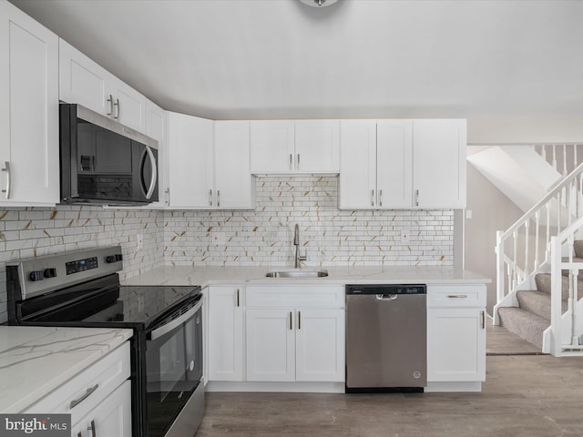 kitchen with sink, light stone counters, appliances with stainless steel finishes, light hardwood / wood-style floors, and white cabinets