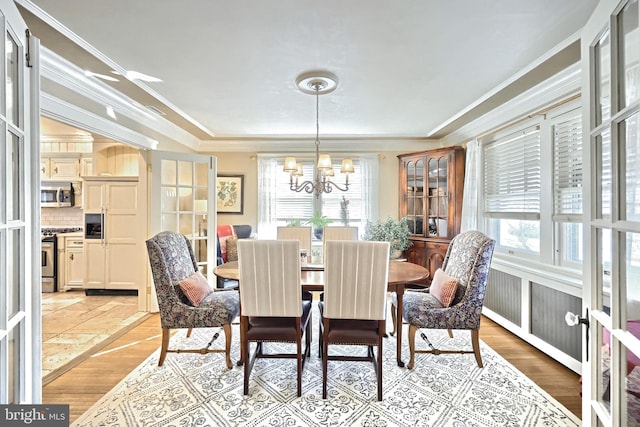 dining space with light hardwood / wood-style flooring, ornamental molding, french doors, and a chandelier