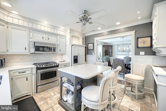 kitchen featuring appliances with stainless steel finishes, white cabinetry, a kitchen breakfast bar, ornamental molding, and ceiling fan with notable chandelier