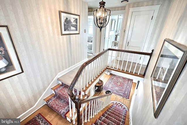 stairway with hardwood / wood-style floors and a notable chandelier