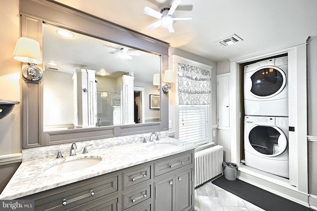 bathroom with stacked washing maching and dryer, radiator, vanity, and ceiling fan