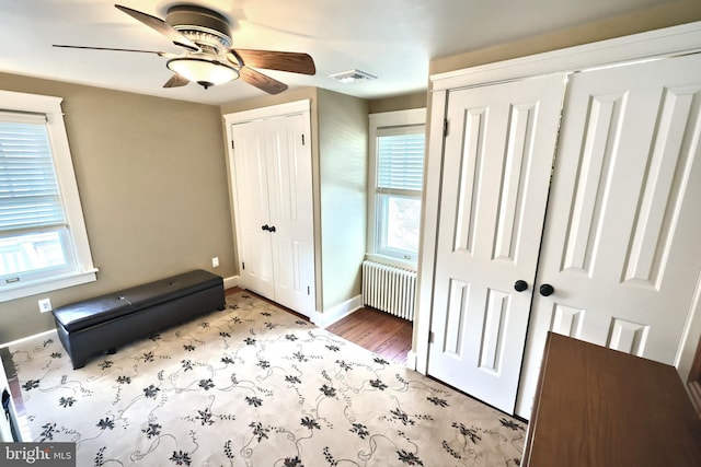 unfurnished bedroom with radiator, two closets, ceiling fan, and light hardwood / wood-style flooring