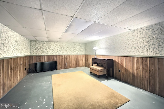 unfurnished room featuring wooden walls, concrete floors, and a drop ceiling