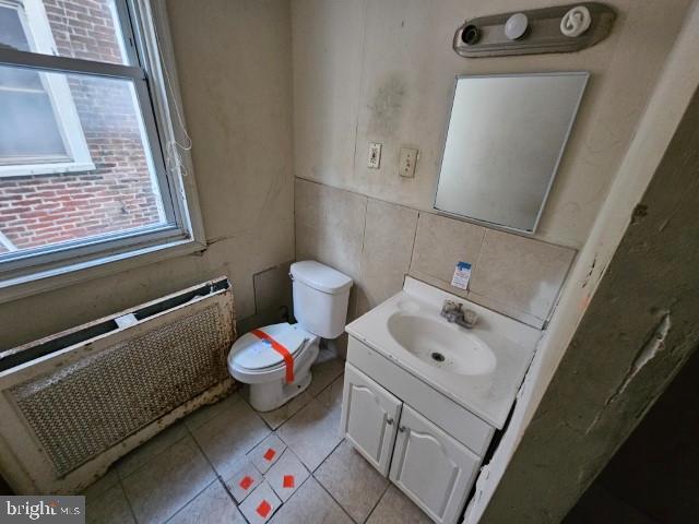 bathroom featuring radiator heating unit, tile walls, tile patterned flooring, vanity, and toilet