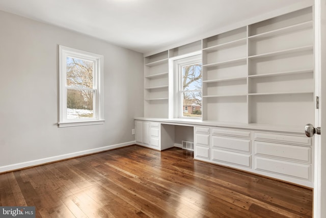 unfurnished office with dark hardwood / wood-style flooring, built in desk, and a healthy amount of sunlight