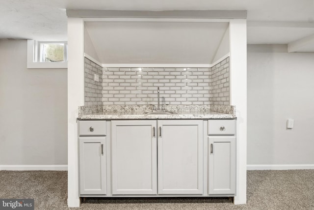 kitchen featuring white cabinetry, light stone countertops, sink, and light carpet