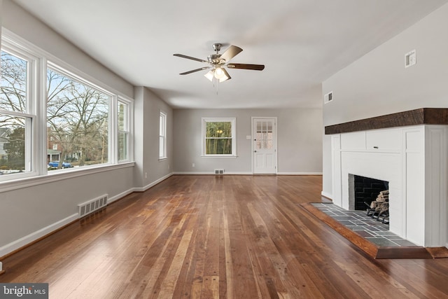 unfurnished living room with dark hardwood / wood-style flooring, a tiled fireplace, and ceiling fan