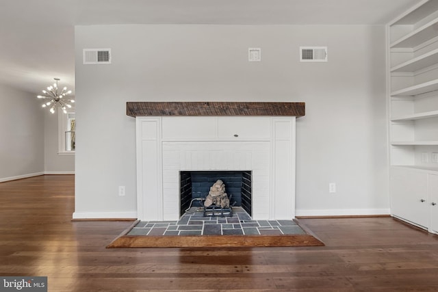 interior details with a brick fireplace, hardwood / wood-style floors, built in features, and an inviting chandelier