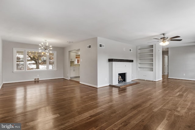 unfurnished living room with built in shelves, dark hardwood / wood-style floors, and ceiling fan with notable chandelier