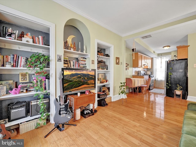 interior space with built in shelves, crown molding, and light wood-type flooring