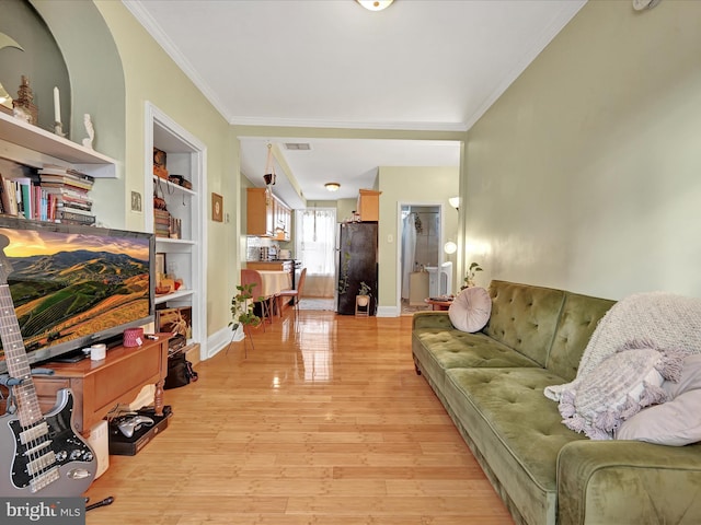 living room featuring ornamental molding, light wood-type flooring, and built in shelves