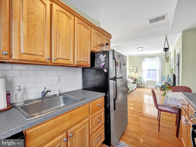 kitchen featuring stainless steel refrigerator, sink, decorative backsplash, crown molding, and light wood-type flooring