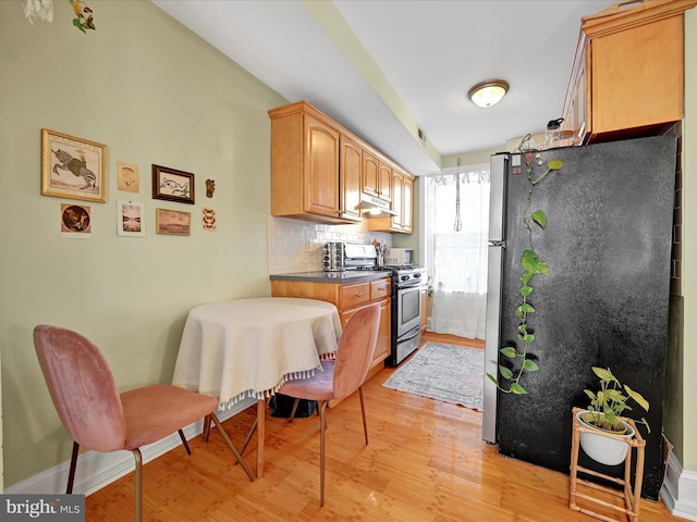 kitchen featuring stainless steel appliances, light brown cabinetry, light hardwood / wood-style floors, and backsplash