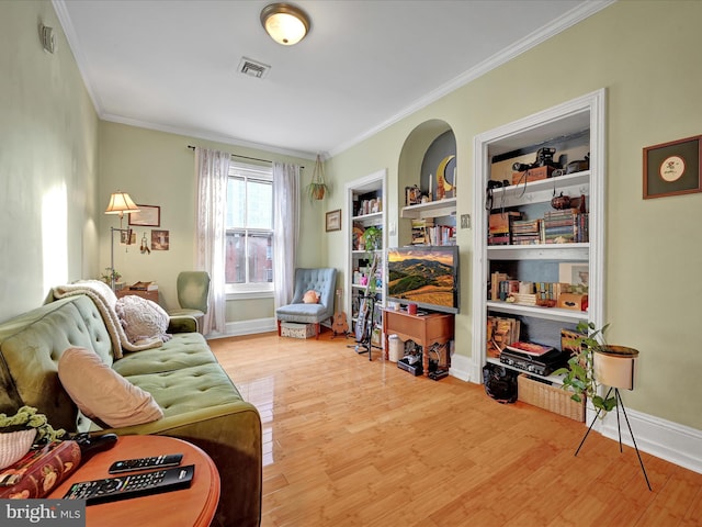 sitting room with crown molding, built in features, and light wood-type flooring