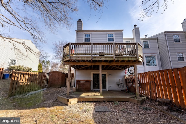 rear view of property featuring a wooden deck, a fenced backyard, a chimney, and a gate