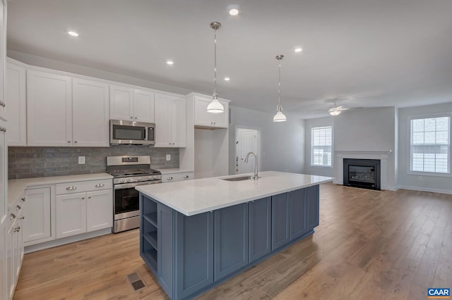 kitchen with pendant lighting, sink, appliances with stainless steel finishes, white cabinets, and a center island with sink