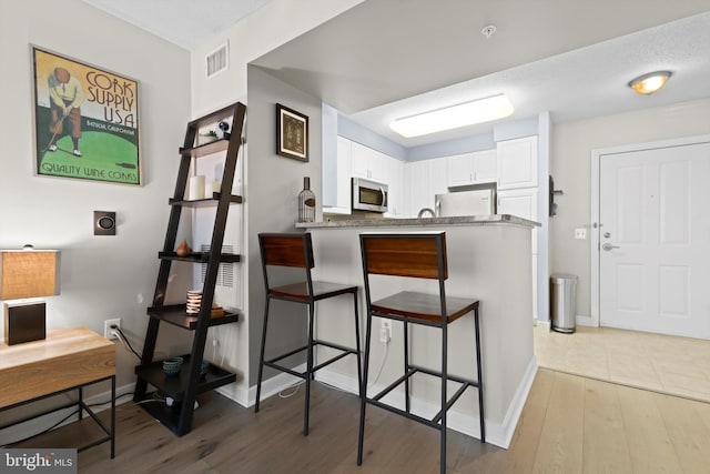 kitchen with hardwood / wood-style flooring, a breakfast bar area, appliances with stainless steel finishes, white cabinetry, and kitchen peninsula