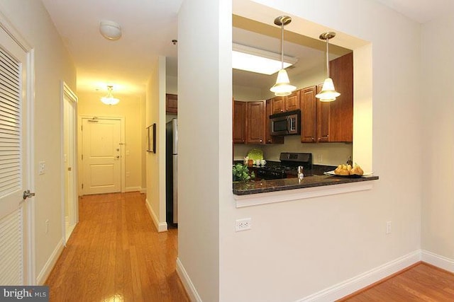 kitchen with stainless steel appliances, kitchen peninsula, light hardwood / wood-style floors, and decorative light fixtures