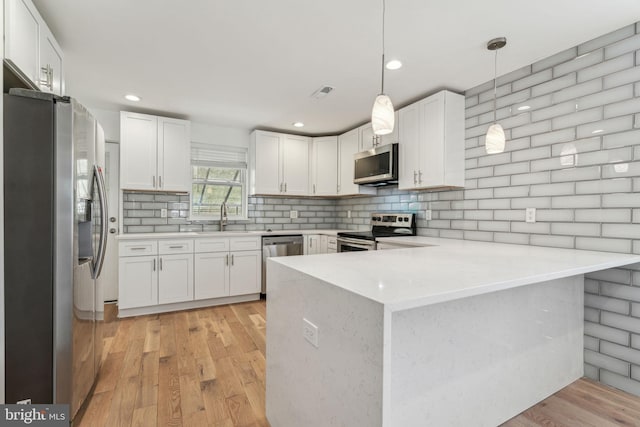 kitchen featuring white cabinetry, decorative light fixtures, kitchen peninsula, stainless steel appliances, and decorative backsplash