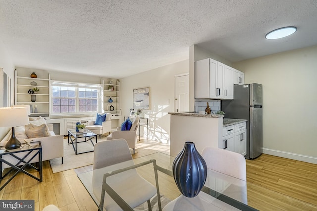 kitchen featuring white cabinetry, light stone countertops, light hardwood / wood-style flooring, and stainless steel refrigerator