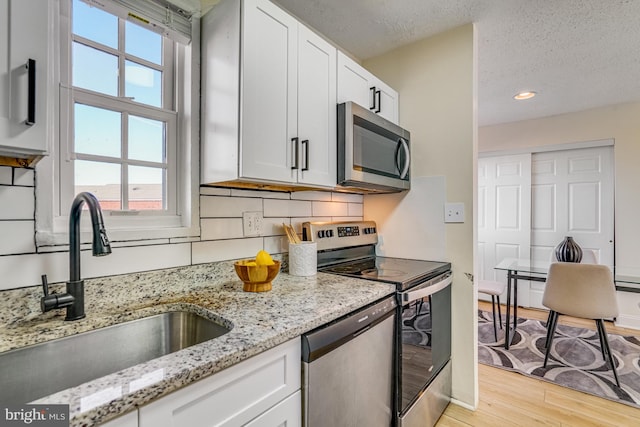 kitchen featuring sink, light hardwood / wood-style flooring, appliances with stainless steel finishes, white cabinetry, and light stone countertops