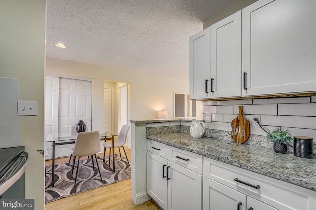 kitchen featuring light wood-type flooring, backsplash, white cabinets, light stone counters, and a textured ceiling