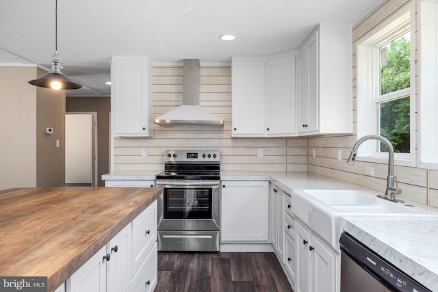 kitchen with pendant lighting, white cabinets, stainless steel appliances, and wall chimney range hood