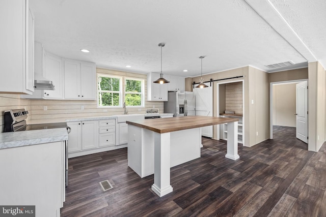 kitchen with butcher block countertops, a center island, appliances with stainless steel finishes, a barn door, and white cabinets