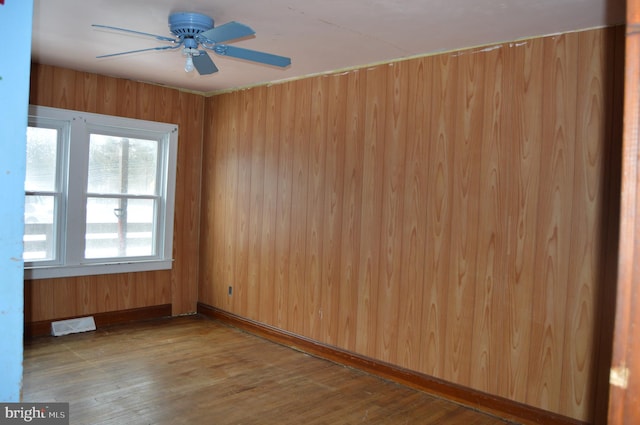 unfurnished room with hardwood / wood-style floors, ceiling fan, and wood walls