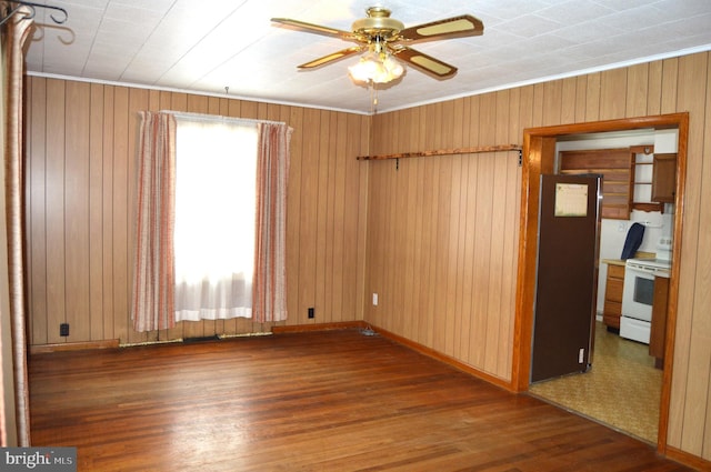 spare room with dark wood-type flooring, ceiling fan, wooden walls, and crown molding