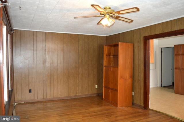 empty room featuring ceiling fan, crown molding, wooden walls, and light hardwood / wood-style floors