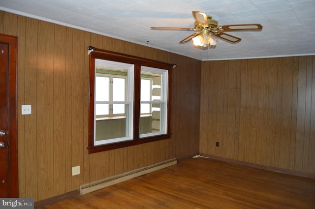 empty room featuring wood-type flooring, wood walls, ceiling fan, and baseboard heating