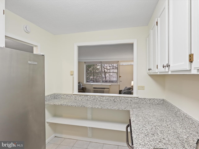 kitchen with white cabinets, stainless steel fridge, light tile patterned floors, light stone counters, and a textured ceiling