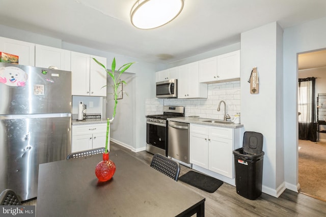 kitchen with tasteful backsplash, white cabinets, appliances with stainless steel finishes, wood finished floors, and a sink